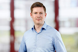 Bewerbungsfotos Hilden. Bewerbungsfoto von einem Mann vor unscharfem Büro Hintergrund.