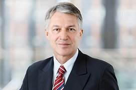 Bewerbungsfotos Hilden. Bewerbungsfoto von einem Mann vor unscharfem Büro Hintergrund.