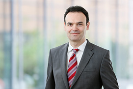 Bewerbungsfotos Hilden. Bewerbungsfoto von einem Mann vor unscharfem Büro Hintergrund.