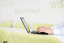 Eine Person am Laptop in einer Corporate Architektur Umgebung. Die Businessfotografie zeigt das entspannte Arbeiten in einer kölner Firma.