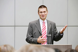 Coach bei einer Rede vor Publikum. Ein Businessfoto mit präziser Handgestik für einen Berater aus Köln.