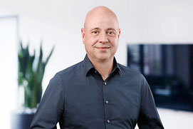 Mitarbeiterfotos Bonn. Mitarbeiterfoto von einem Mann vor unscharfem Büro Hintergrund für ein Unternehmen.