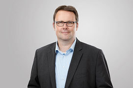 Mitarbeiterfotos Dortmund. Lockeres Mitarbeiterportrait von einem Mann vor grauem Hintergrund für ein Unternehmen.
