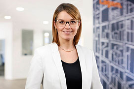 Mitarbeiterfotos Dortmund. Entspanntes Mitarbeiterportrait von einer Frau vor unscharfem Büro Hintergrund für ein Unternehmen.
