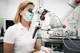 Eine Zahnärztin aus Köln blickt durch ein Mikroskop bei der Behandlung. Praxisfotos in Köln, Bonn, Düsseldorf und NRW.
